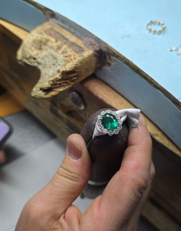 Jeweler hand-setting an emerald and diamond halo engagement ring at the workbench - Nikita Jewelry atelier